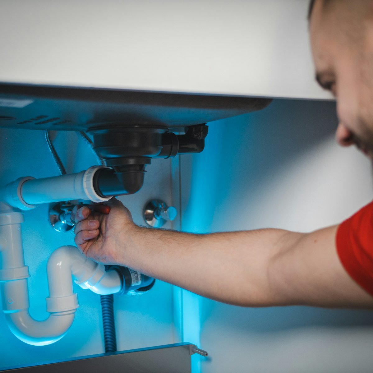 Engineer repairing exposed pipework set into a wall, hands and tools visible with the pipework as the main focus